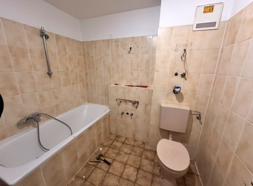 Badezimmer mit Badewanne, Toilette und beige gefliesten Wänden.